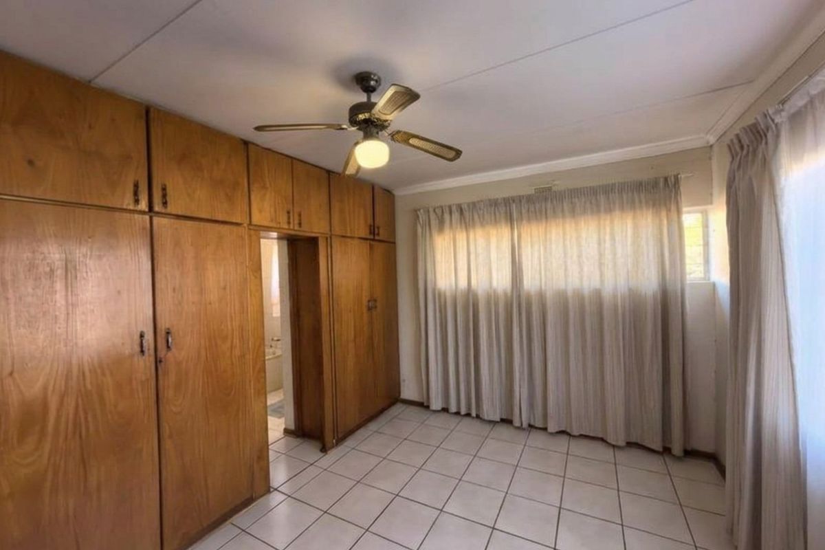 A bedroom featuring built-in wooden cupboards, tiled flooring, and a ceiling fan, offering a functional space ready for personalization.