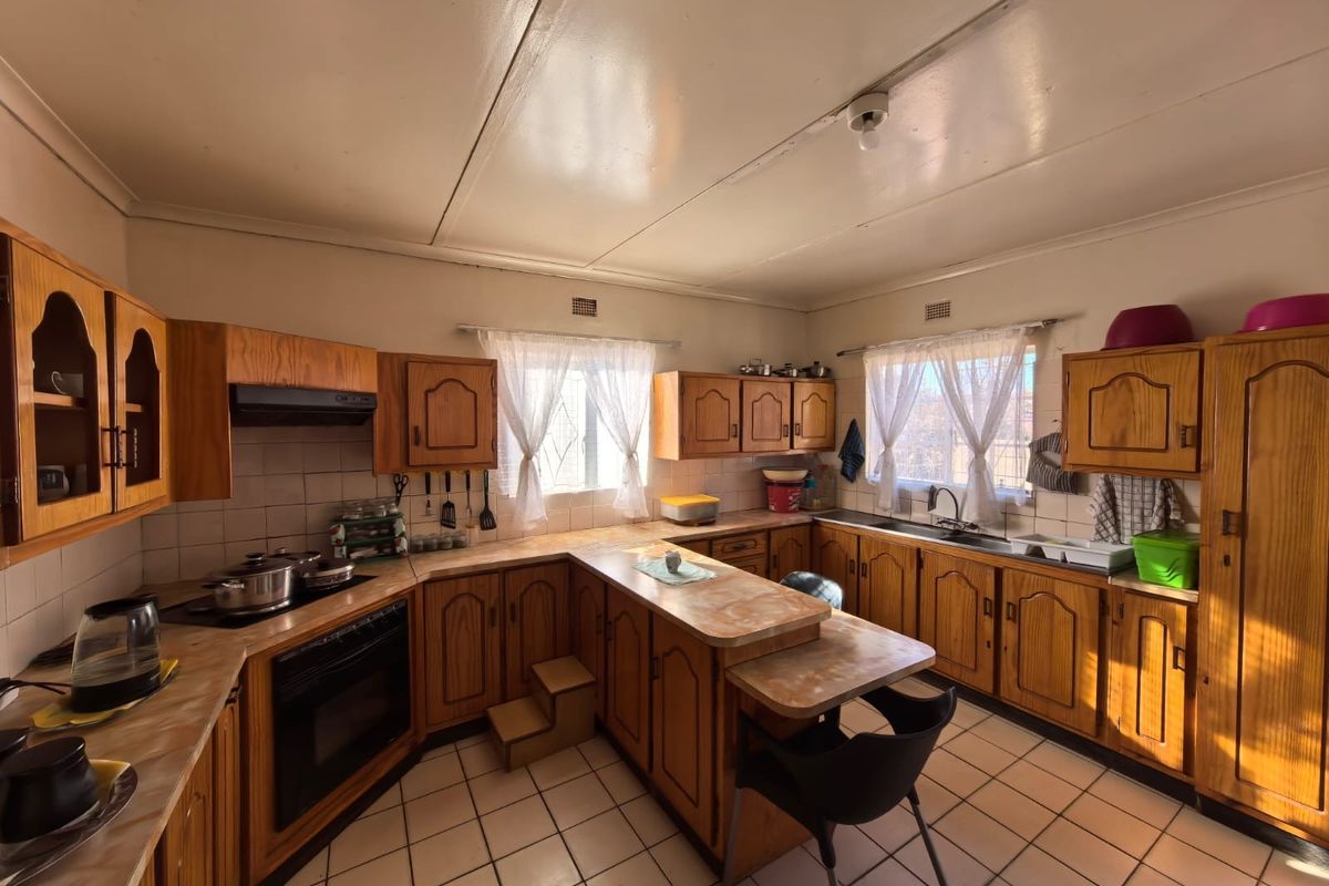 A spacious kitchen featuring traditional wooden cabinetry, laminate countertops, built-in oven, extractor fan, and tiled flooring, offering a functional layout with ample storage.