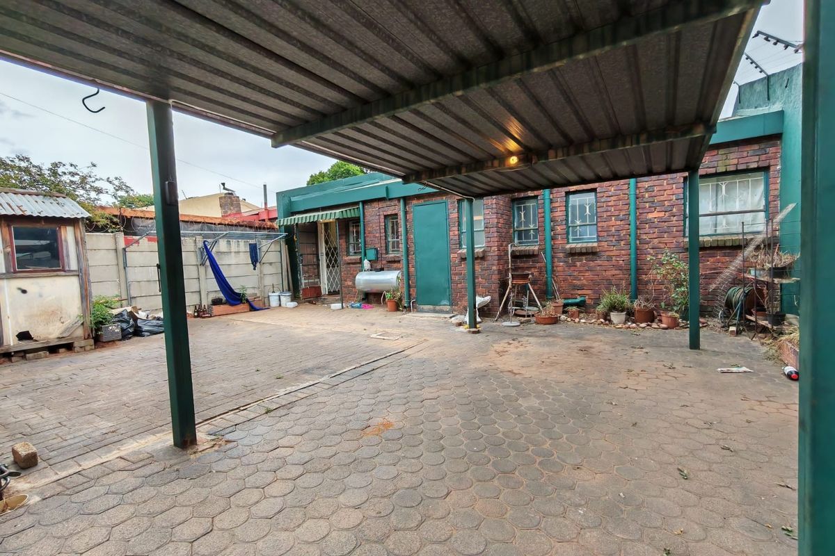 Rear exterior view of the property featuring a paved courtyard, brick facade, and a functional metal carport structure.