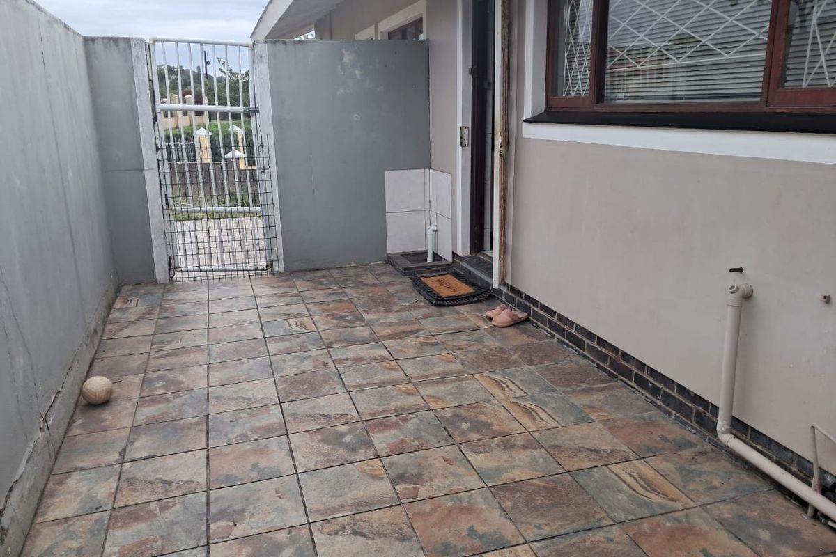 A paved rear courtyard area featuring a security gate, external plumbing access, and boundary walls, providing a functional outdoor utility space.
