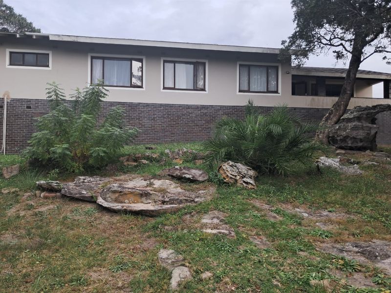 Rear view of the house featuring a combination of brick and plastered walls with casement windows and a natural, rocky garden setting.