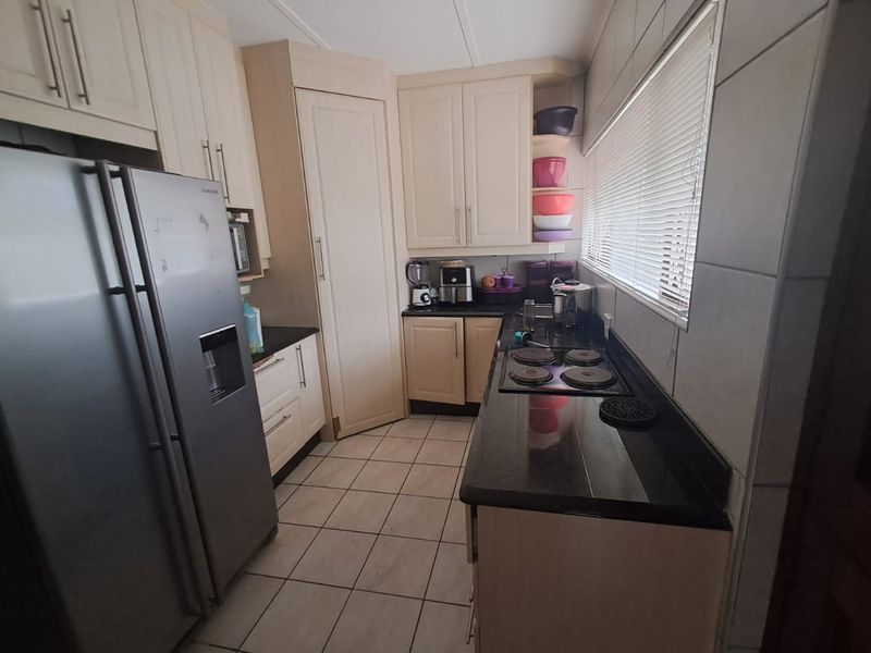 A functional kitchen featuring cream-colored cabinetry, black granite countertops, an electric hob, and tiled flooring, offering a practical layout for daily meal preparation.