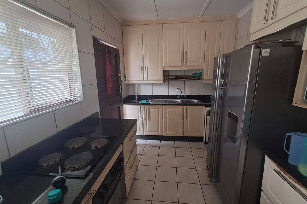 A functional kitchen featuring granite countertops, built-in cabinetry, an electric hob, and tiled flooring, offering a practical layout for daily meal preparation.