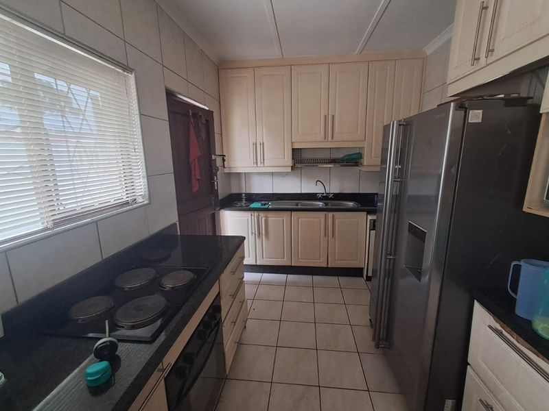 A functional kitchen featuring granite countertops, built-in cabinetry, an electric hob, and tiled flooring, offering a practical layout for daily meal preparation.