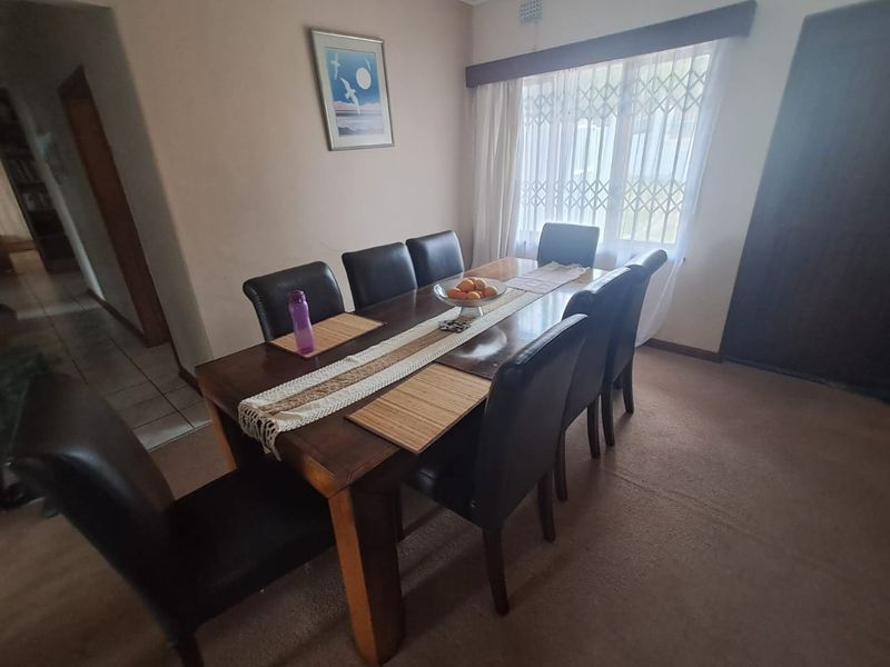 A functional dining room featuring neutral wall finishes, carpeted flooring, and a window fitted with a security gate.