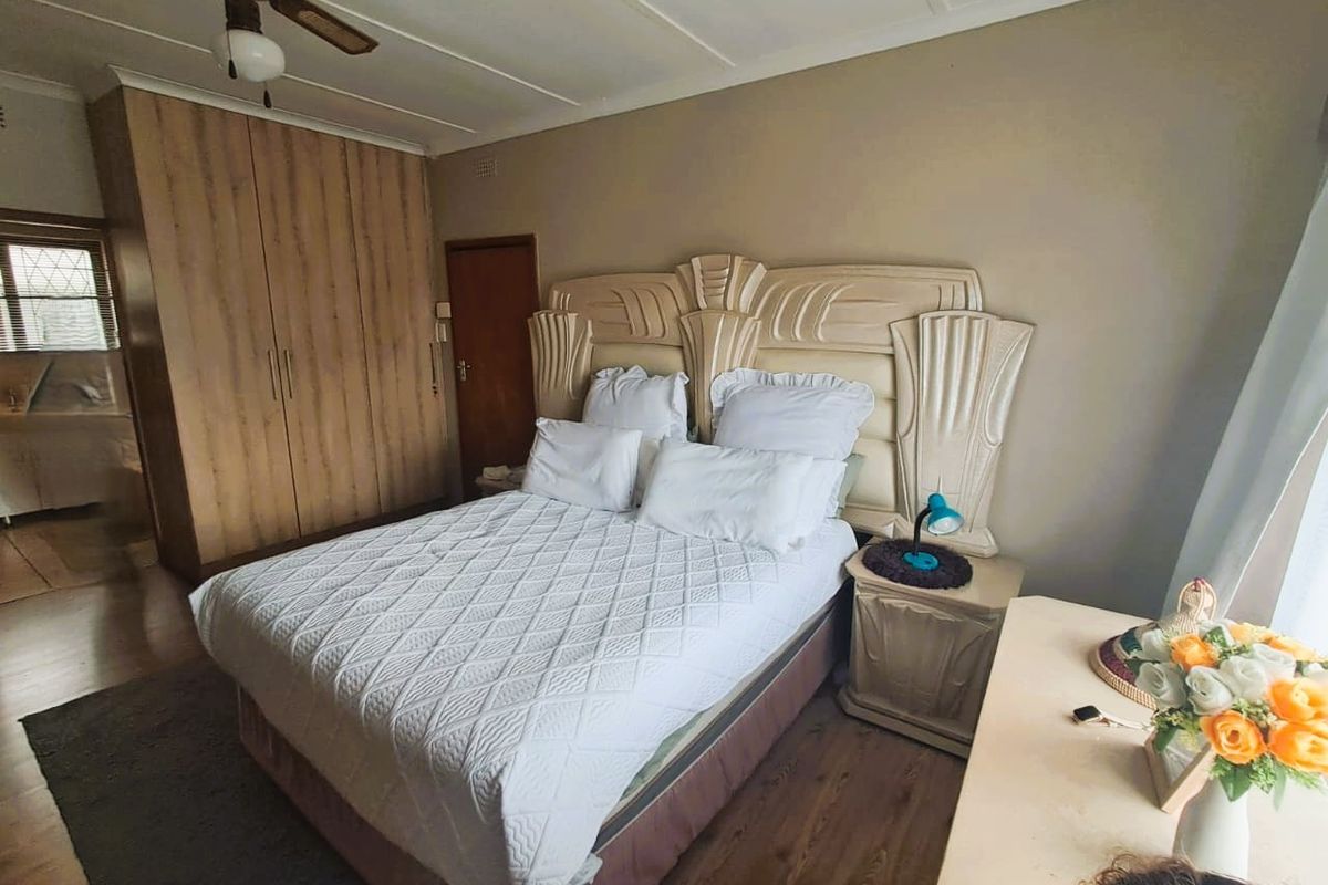 A bedroom featuring built-in wooden wardrobes, laminate flooring, and a ceiling fan, offering a functional and comfortable living space.