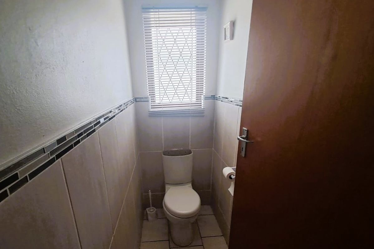 A compact guest bathroom featuring tiled walls and flooring, equipped with a standard toilet and a window with security bars.