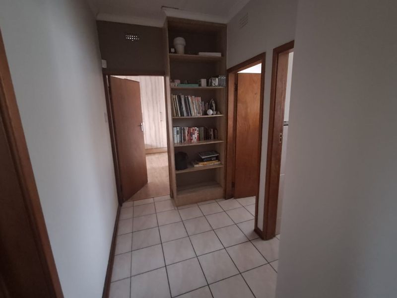 A functional hallway featuring tiled flooring and a built-in wooden shelving unit, providing access to multiple rooms within the home.