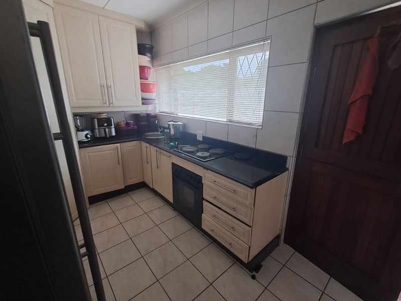 A functional kitchen featuring built-in cabinetry, stone countertops, an integrated oven and hob, and tiled finishes throughout.