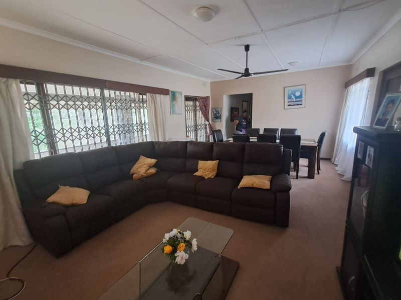 Spacious open-plan living and dining area featuring carpeted flooring, a ceiling fan, and large sliding doors with security gates.