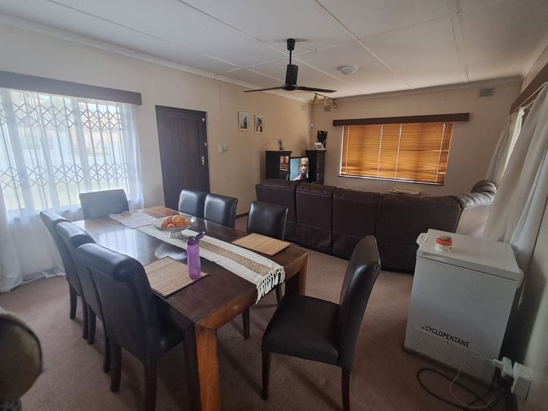 Open plan living and dining area featuring carpeted flooring, ceiling fan, and security gates on windows, offering a functional layout for family living.