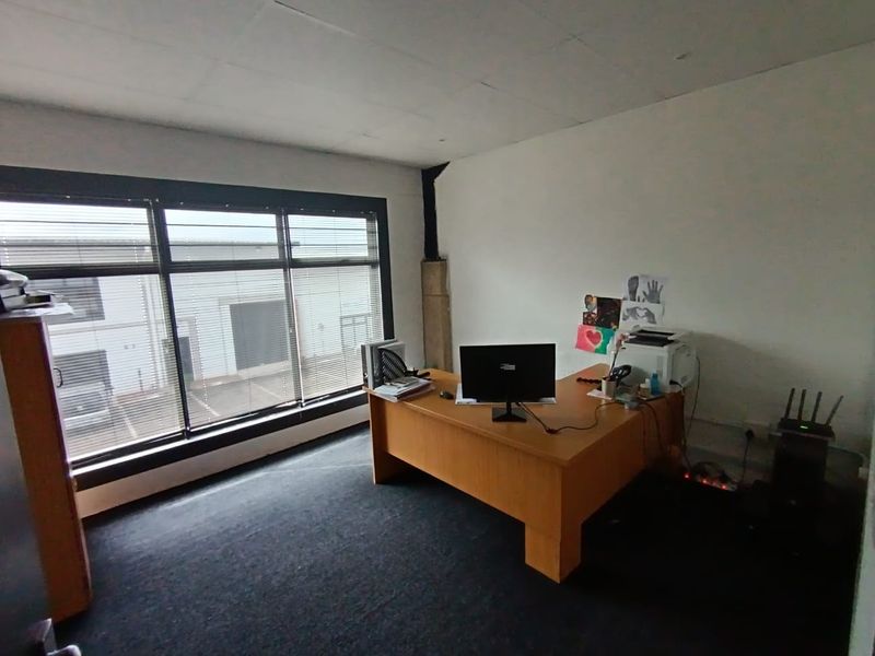 A functional office space featuring large windows with venetian blinds, carpeted flooring, and a suspended ceiling, suitable for a professional work environment.