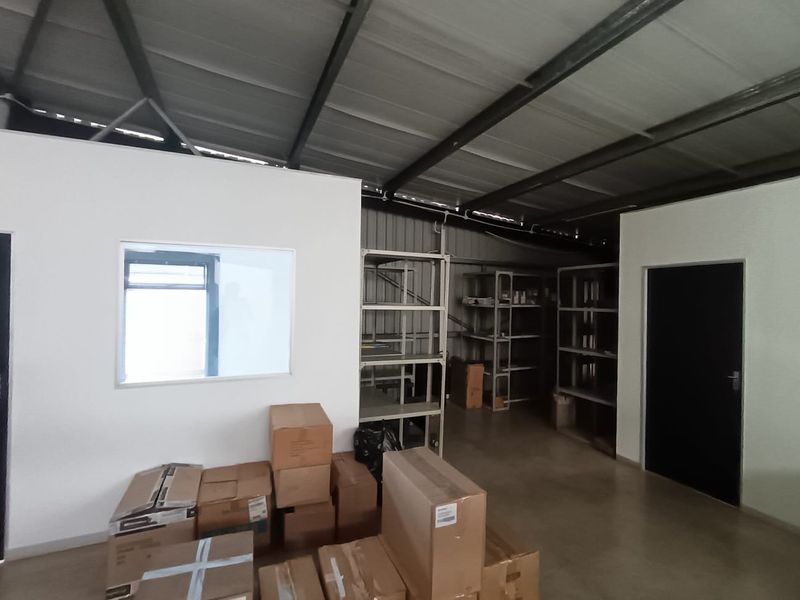 A functional utility or storage space featuring exposed steel roof trusses, concrete flooring, and built-in metal shelving units.
