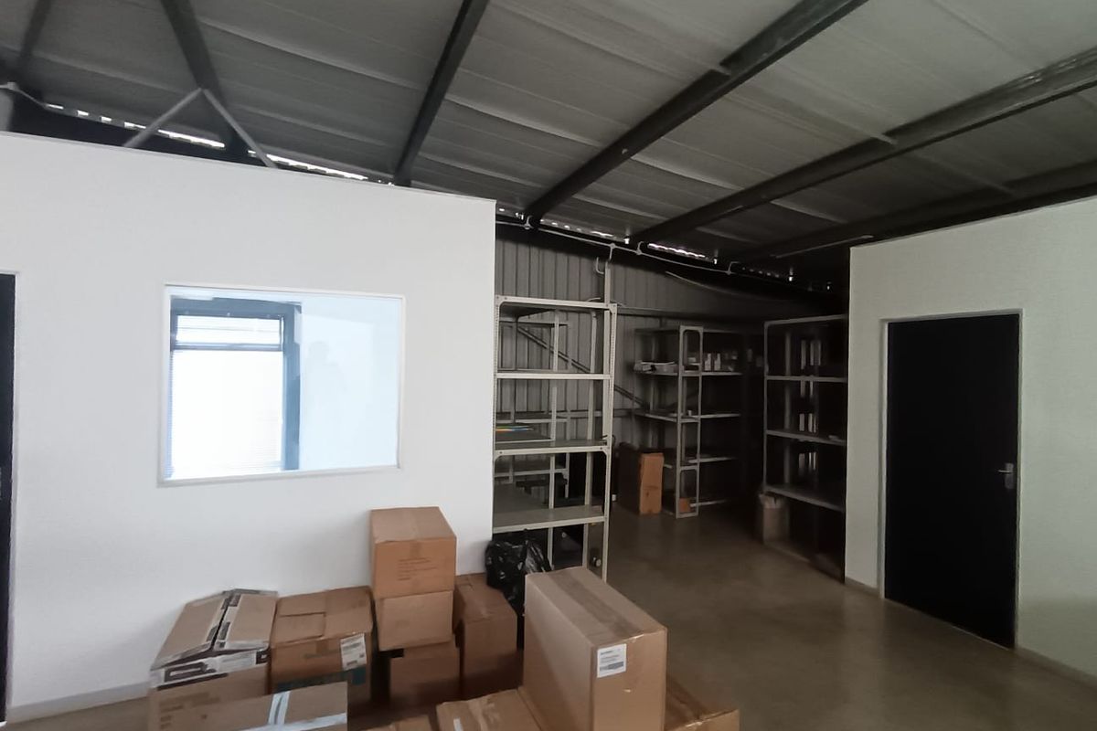 A functional utility or storage space featuring exposed steel roof trusses, concrete flooring, and built-in metal shelving units.