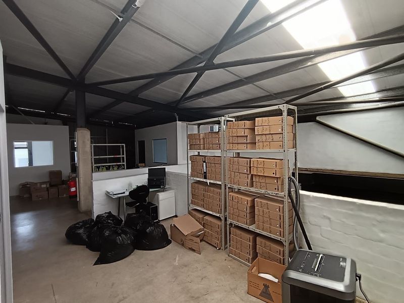 A functional utility or storage space featuring exposed steel roof trusses, concrete flooring, and natural light provided by a skylight.