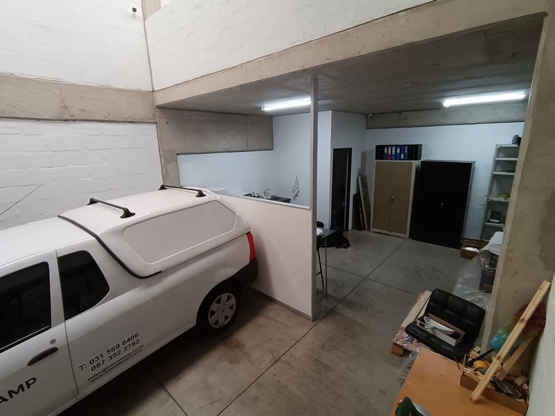 A functional commercial garage space featuring exposed concrete structural elements, a partition wall, and a small integrated sink area.