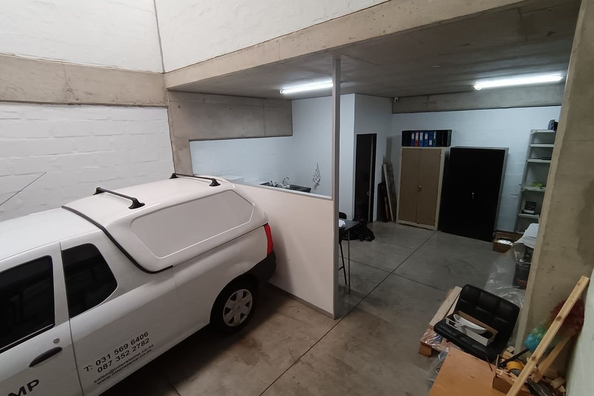 A functional commercial garage space featuring exposed concrete structural elements, a partition wall, and a small integrated sink area.
