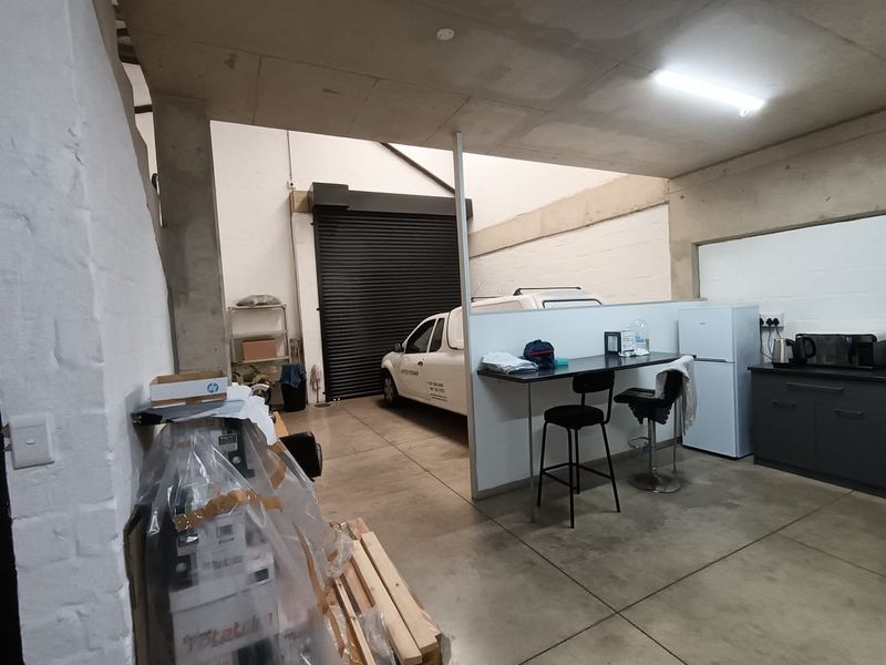 A functional commercial utility space featuring concrete flooring, exposed ceiling, and a large roller shutter door for vehicle or equipment access.