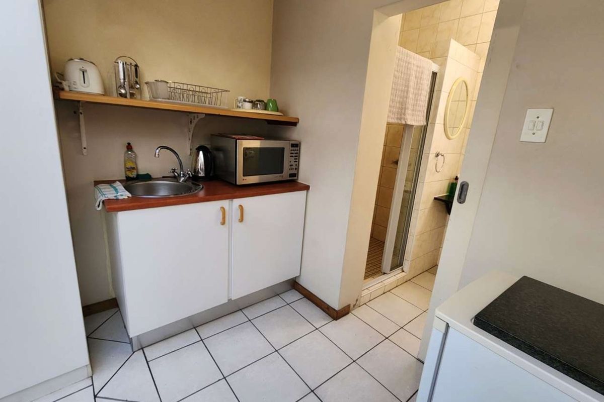 Compact kitchenette featuring white cabinetry, a sink, and tiled flooring, with direct access to an adjacent bathroom.
