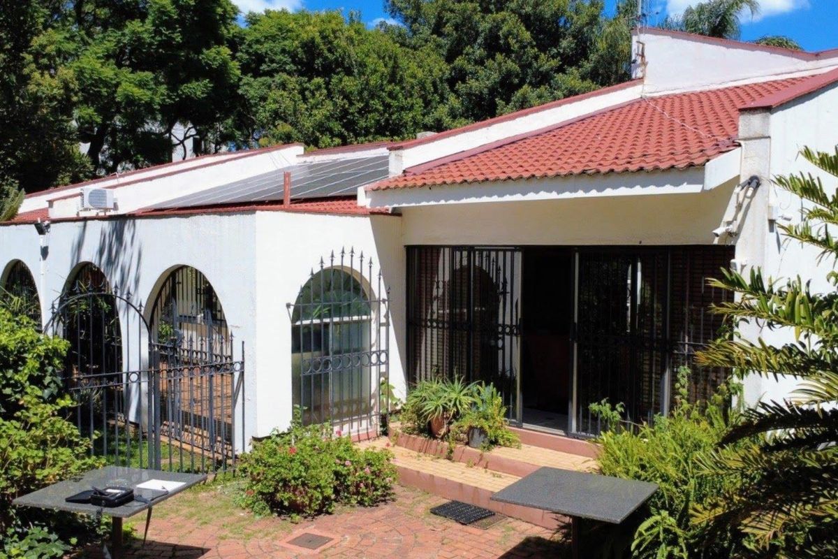 Rear view of the property featuring a tiled roof, solar panels, arched window detailing, security gates, and a brick-paved patio area.