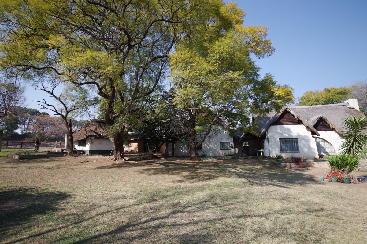 A view of the rear farmstead featuring traditional thatched roof structures, masonry walls, and established trees set within a large garden area.