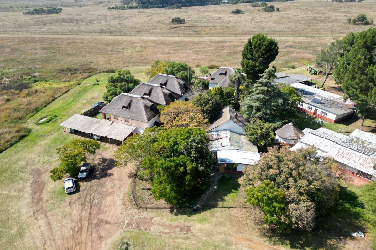 Aerial view of a small holding property featuring multiple structures with thatched roofs, a large carport, and expansive surrounding grounds.
