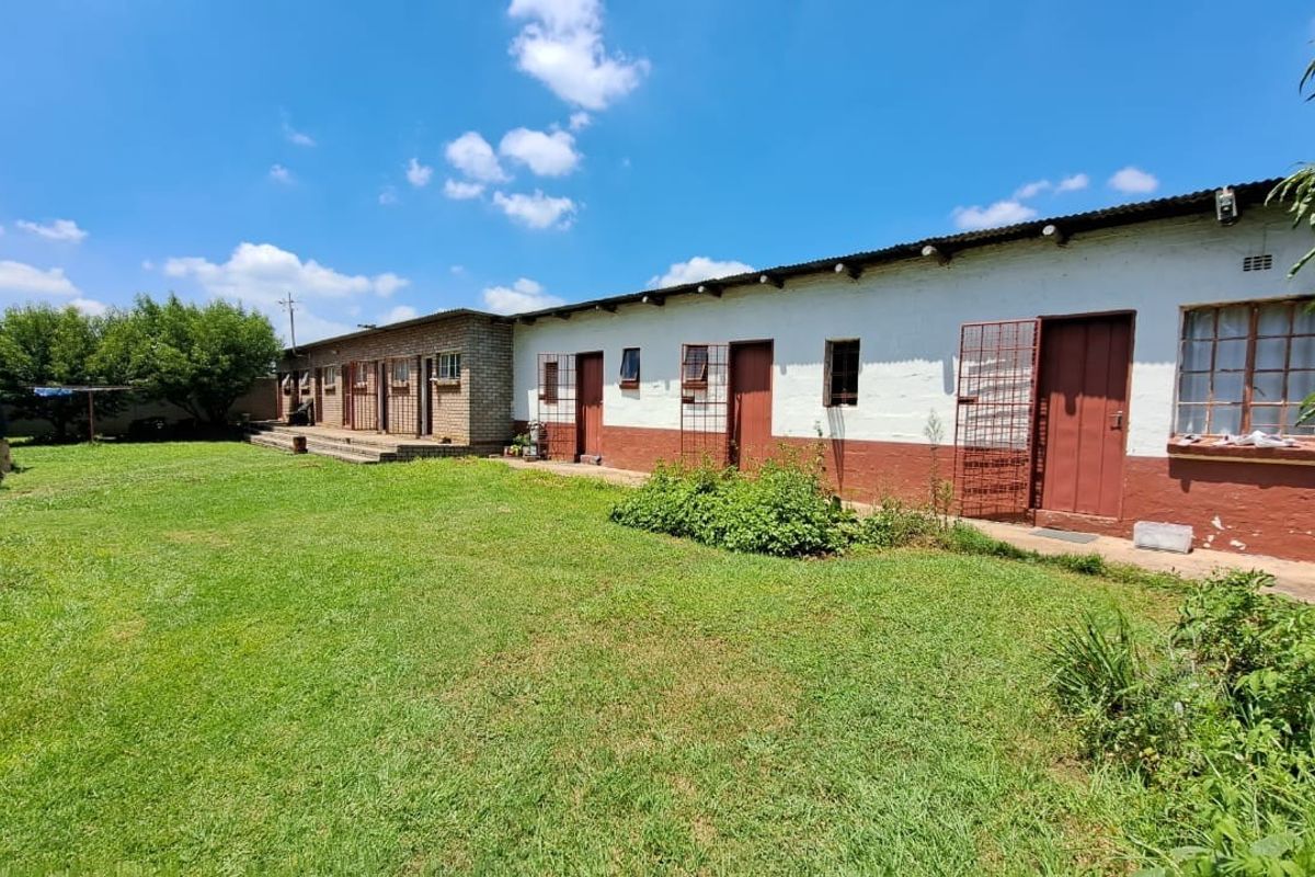 Rear view of a small holding property featuring a long building with multiple entrances, security gates, and a large grass garden area.