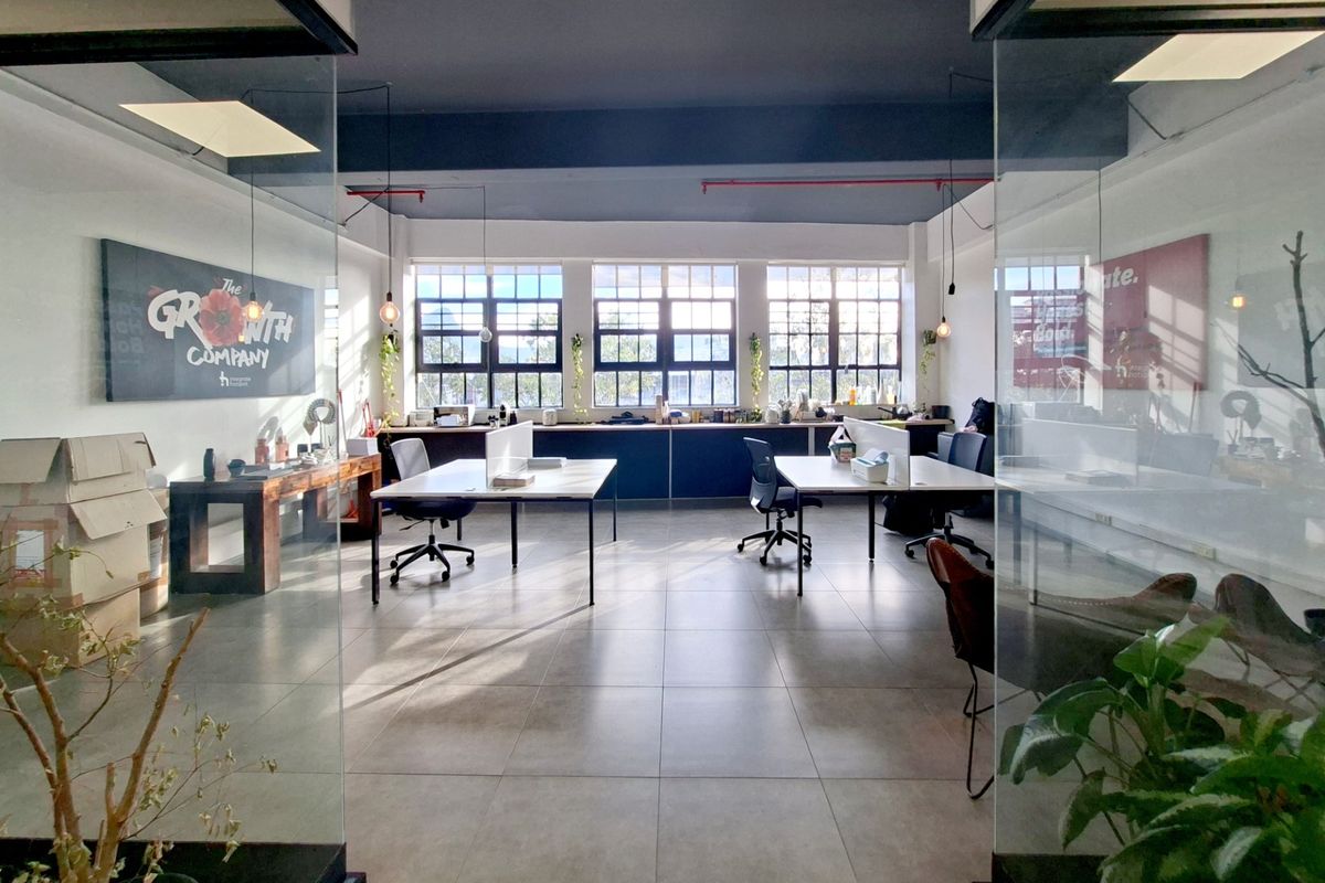A bright, open-plan office space featuring large industrial windows, tiled flooring, and modern glass partitions, providing a professional and airy work environment.