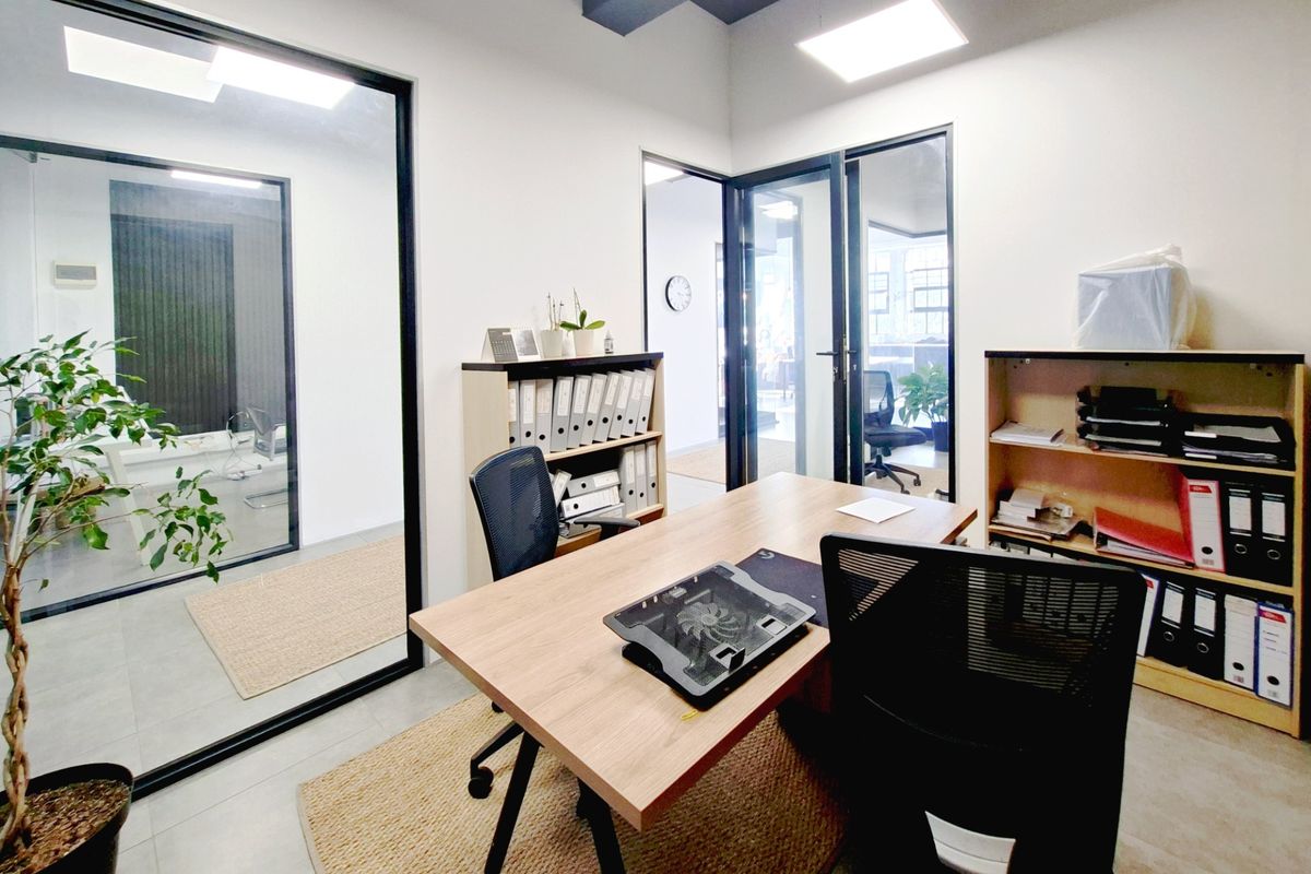 A modern office space featuring glass partition walls, black aluminum framing, recessed LED lighting, and clean tiled flooring.