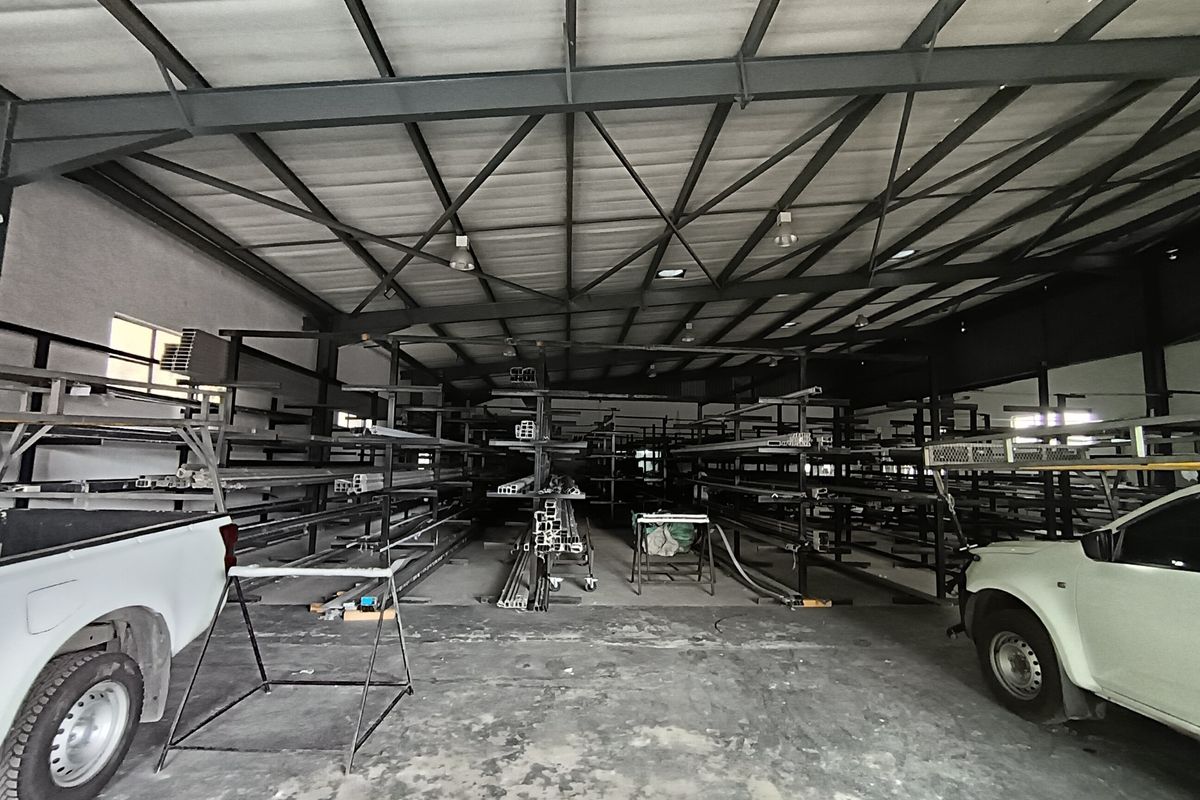 Spacious industrial warehouse featuring high-clearance exposed steel roof trusses, concrete flooring, and extensive built-in metal racking systems for storage.