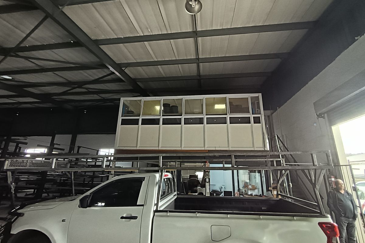 Industrial warehouse space featuring high exposed steel roof trusses and a built-in mezzanine office enclosure.