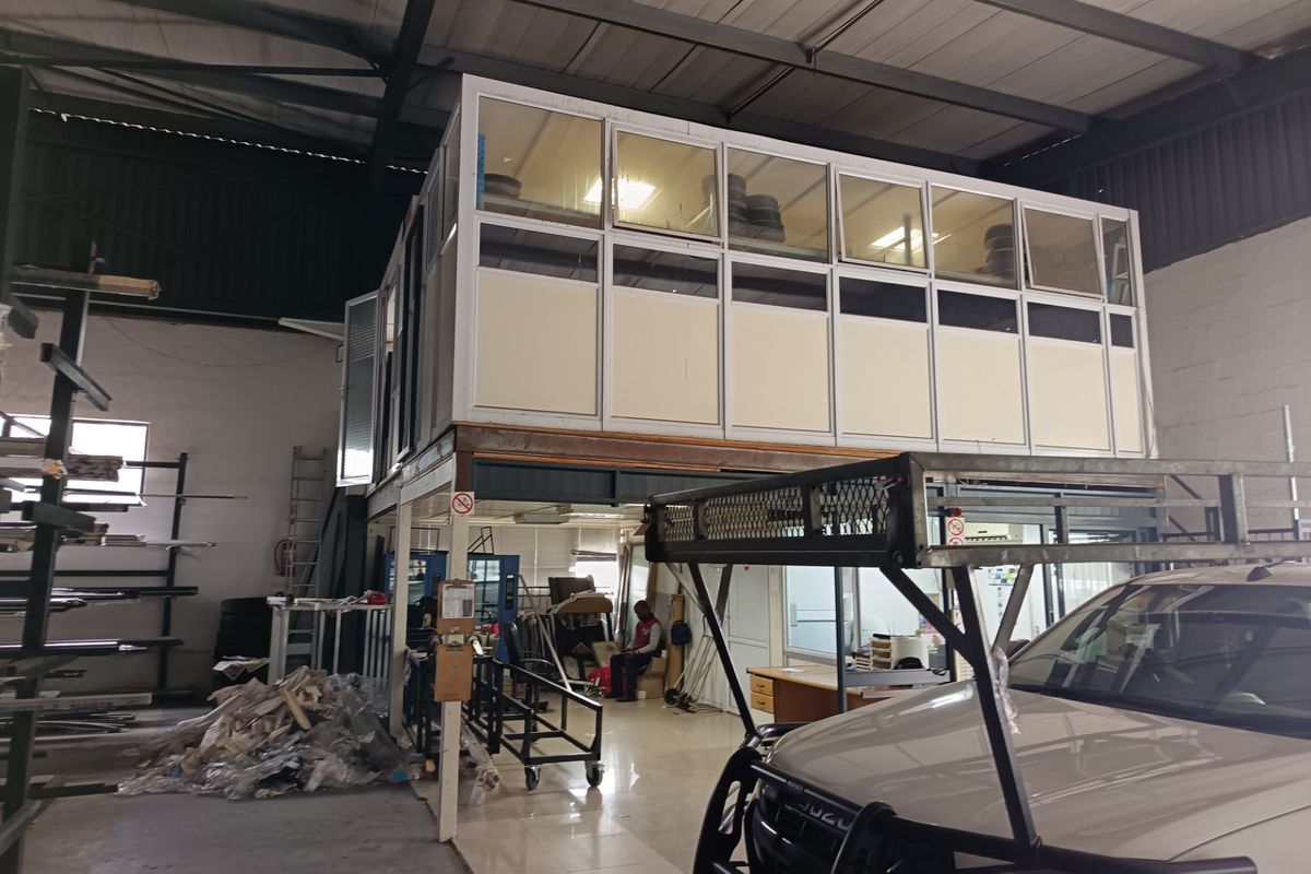 Industrial warehouse space featuring a raised mezzanine office structure with aluminum framing and tiled flooring, suitable for versatile commercial or storage use.