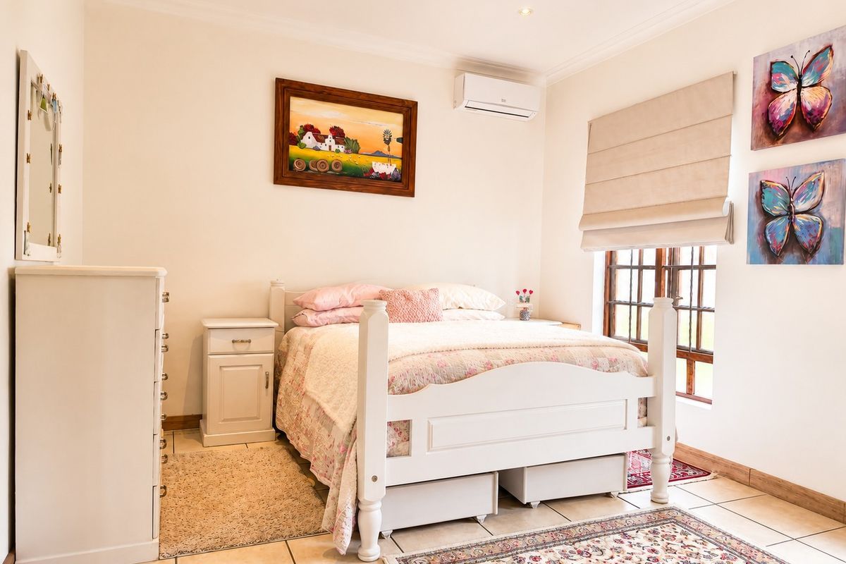 A well-maintained bedroom featuring tiled flooring, an integrated air conditioning unit, and a window with a fitted roman blind.