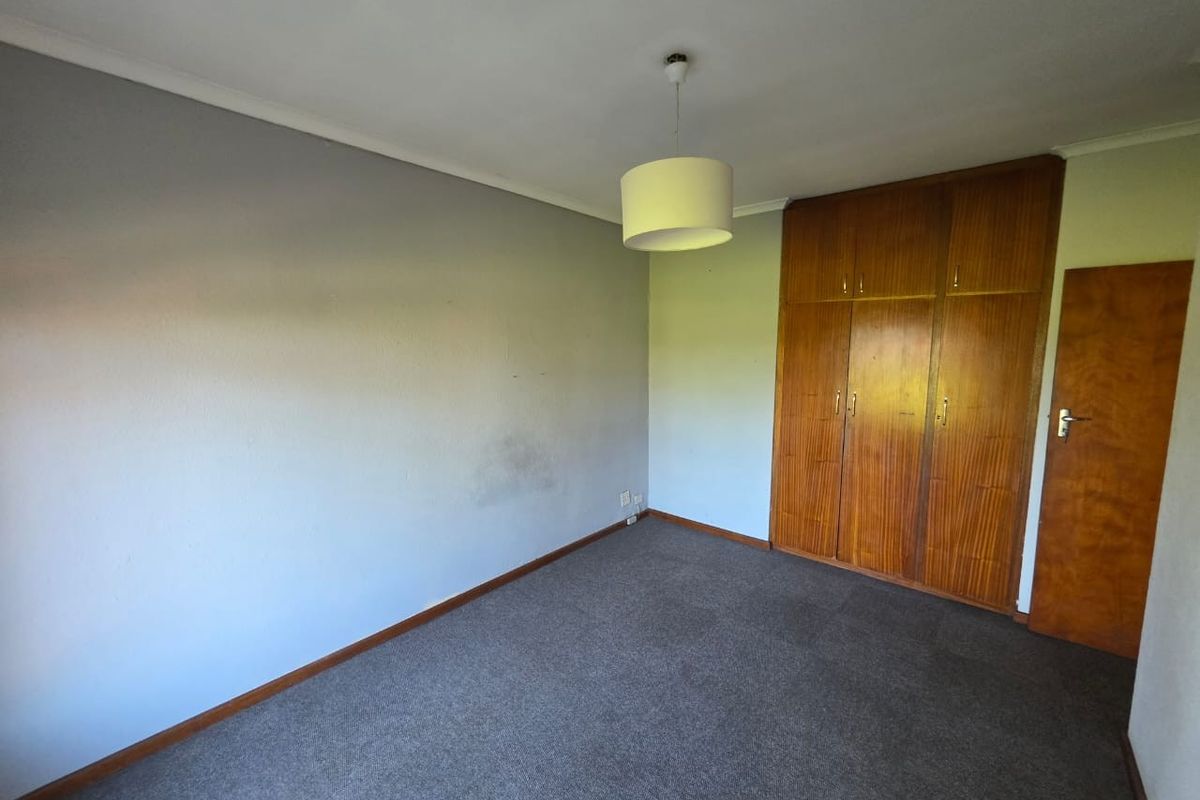 An empty bedroom featuring built-in wooden wardrobes, grey carpeting, and a neutral wall finish, ready for personalization.