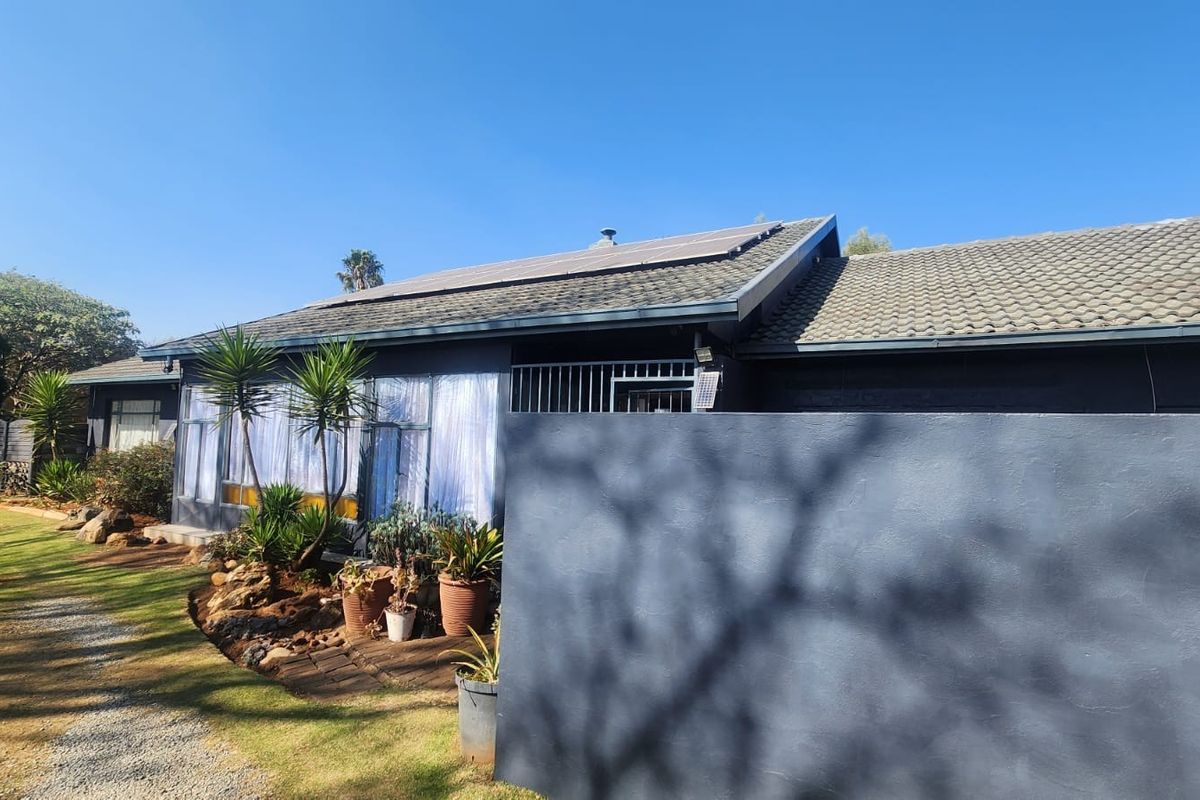 Rear view of the property featuring a tiled roof with installed solar panels, a secure entrance gate, and a painted boundary wall.