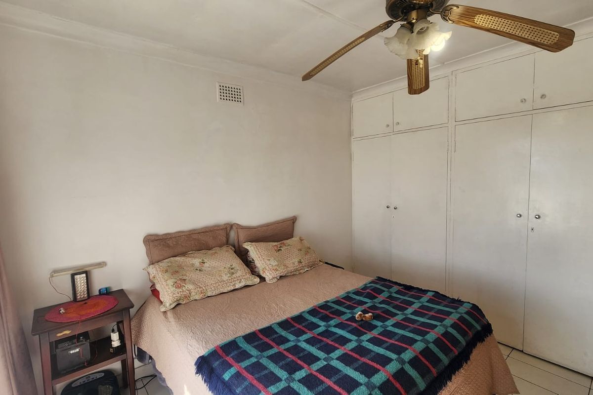 A bedroom featuring built-in cupboards, a ceiling fan, and tiled flooring, offering a functional space with potential for cosmetic updates.