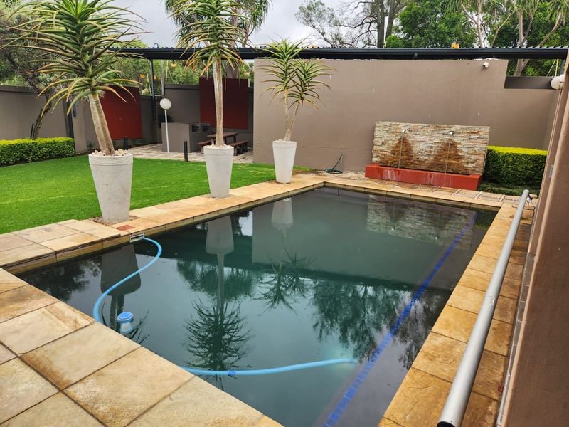Outdoor pool area featuring a stone water feature, paved surround, and landscaped lawn, enclosed by a boundary wall.