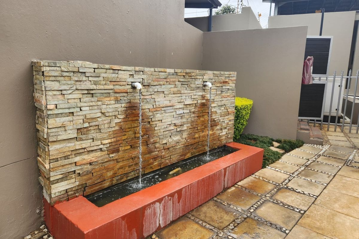 A rear outdoor area featuring a stone-clad water feature with a paved patio and boundary wall.