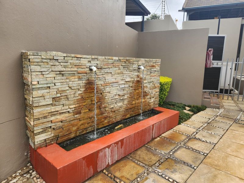 A rear outdoor area featuring a stone-clad water feature with a paved patio and boundary wall.