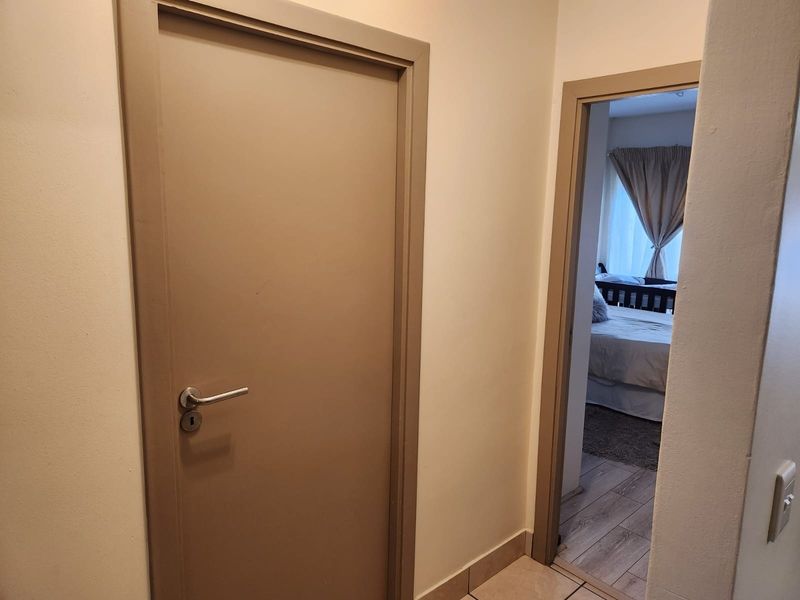 A functional hallway area featuring neutral painted walls, internal doors, and a transition between tiled and laminate flooring leading into a bedroom.