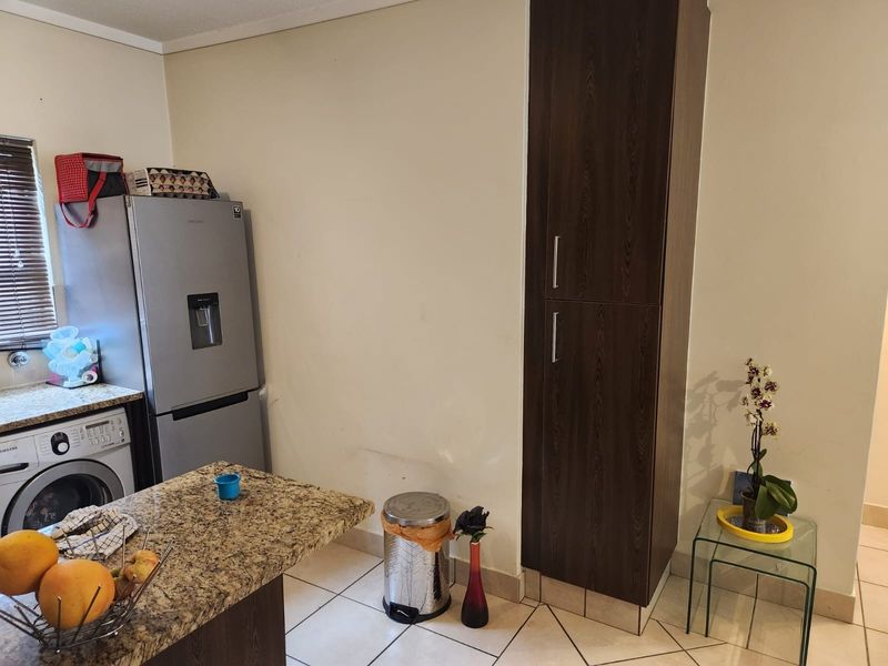 A functional kitchen area featuring granite countertops, tiled flooring, and a tall built-in dark wood pantry cupboard.