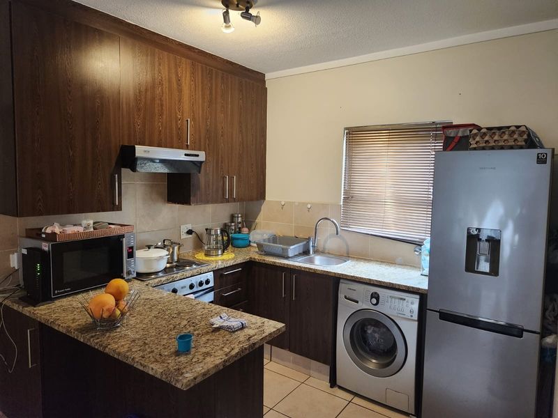 A functional kitchen featuring dark wood cabinetry, granite countertops, a tiled backsplash, and integrated space for laundry appliances.