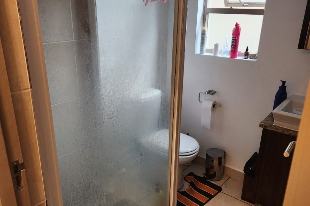 A compact bathroom featuring a shower enclosure, toilet, and vanity basin with tiled finishes and a top-hung window for ventilation.