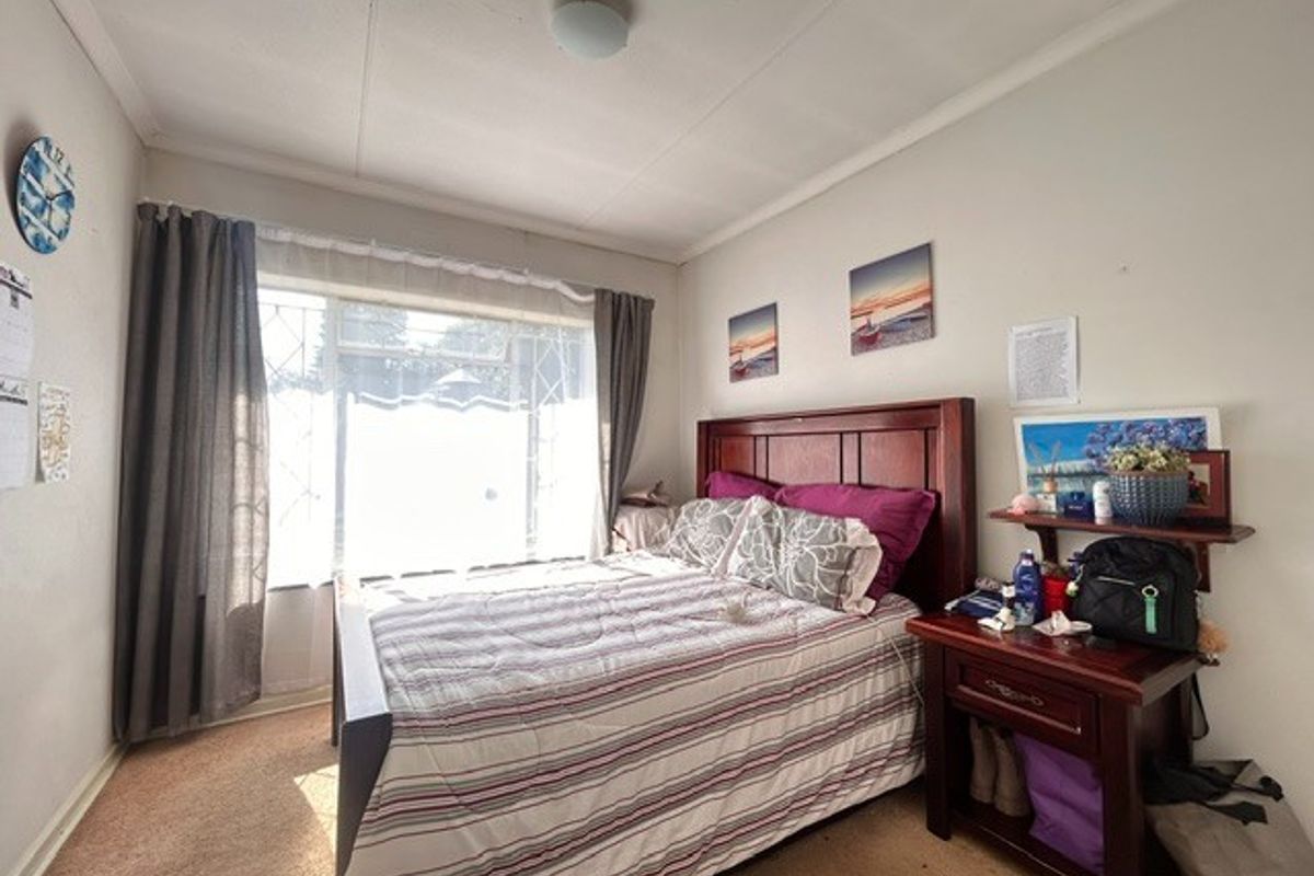 A standard bedroom featuring carpeted flooring, a large window providing natural light, and a neutral wall finish.