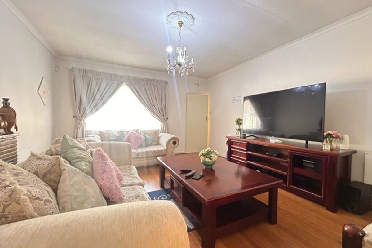 A comfortable living room featuring polished hardwood flooring, a decorative ceiling rose, and a classic chandelier, providing a warm and inviting atmosphere.