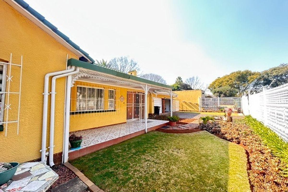 Rear view of the property featuring a covered patio with decorative ironwork, tiled flooring, and a well-maintained garden area.