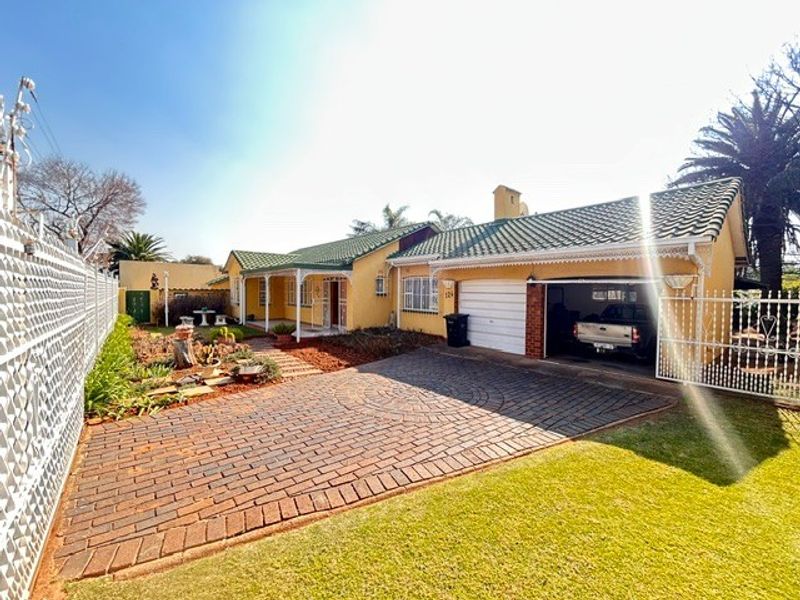 Front view of a single-story house featuring a paved driveway, attached garage, covered porch, and well-maintained garden area.