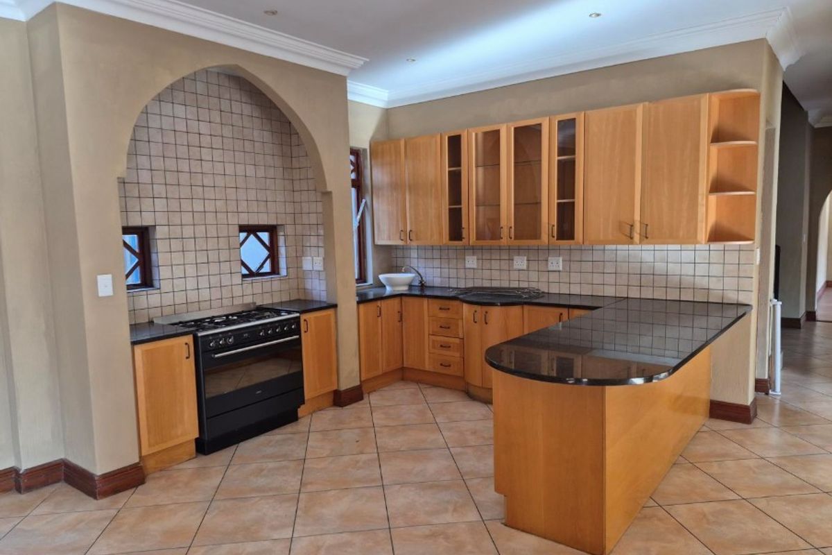 Spacious kitchen featuring wooden cabinetry, granite countertops, a built-in oven and hob, and a distinctive arched alcove with tiled splashback.