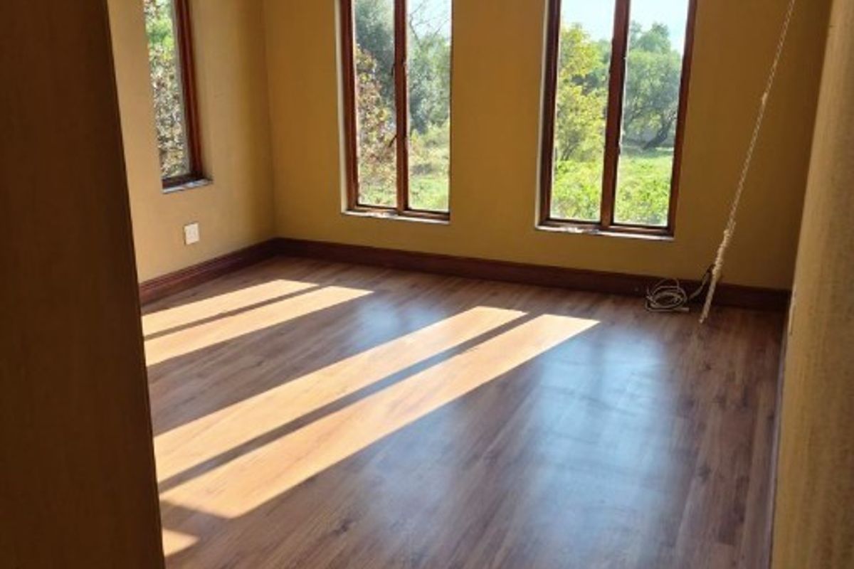A bright, empty bedroom featuring distinctive gothic arch windows, warm-toned laminate flooring, and neutral wall finishes, offering a peaceful view of the surrounding greenery.