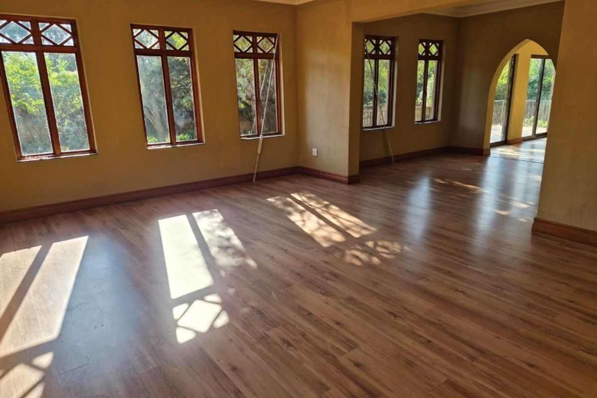 Spacious, empty living area featuring warm-toned laminate flooring, timber-framed windows, and a classic architectural archway leading to an adjoining space.